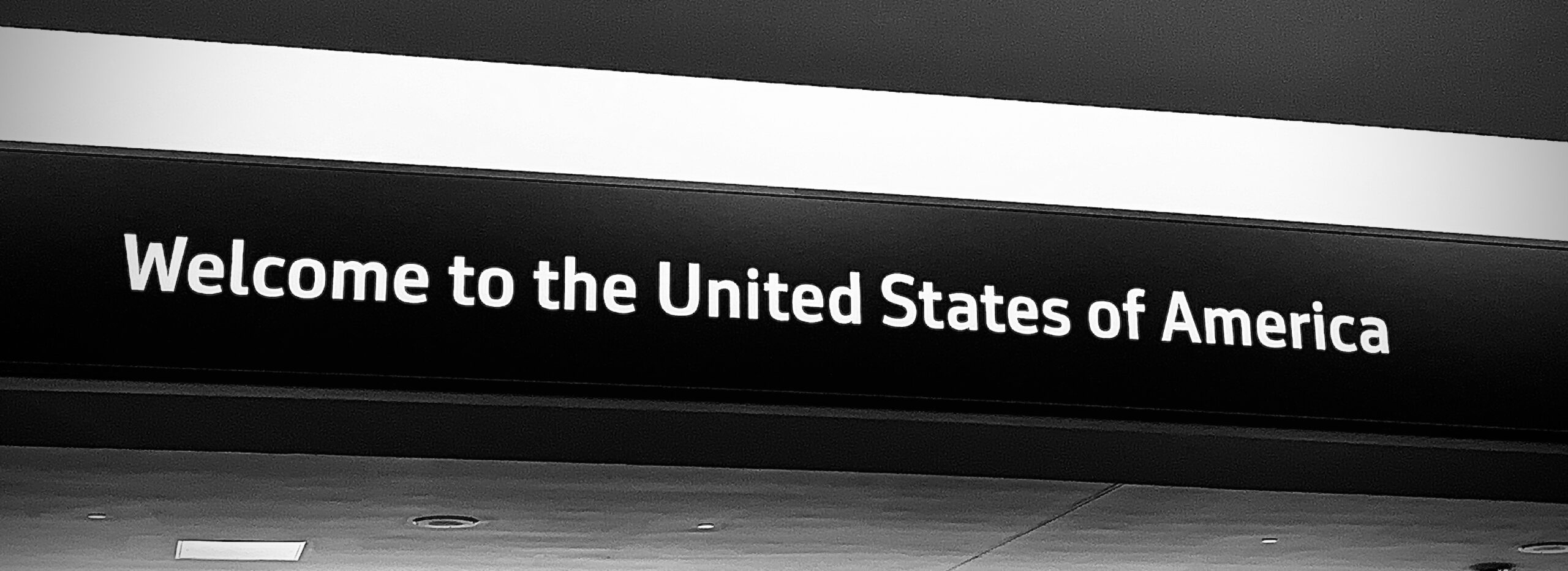 Cartello aeroportuale bianco e nero che recita "Welcome to the United States of America", segno ufficiale di benvenuto negli Stati Uniti all'arrivo in aeroporto