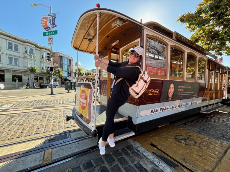 Alessia di Red Lace sorrride e saluta con la mano dal Cable Car numero 28 di San Francisco su una strada acciottolata