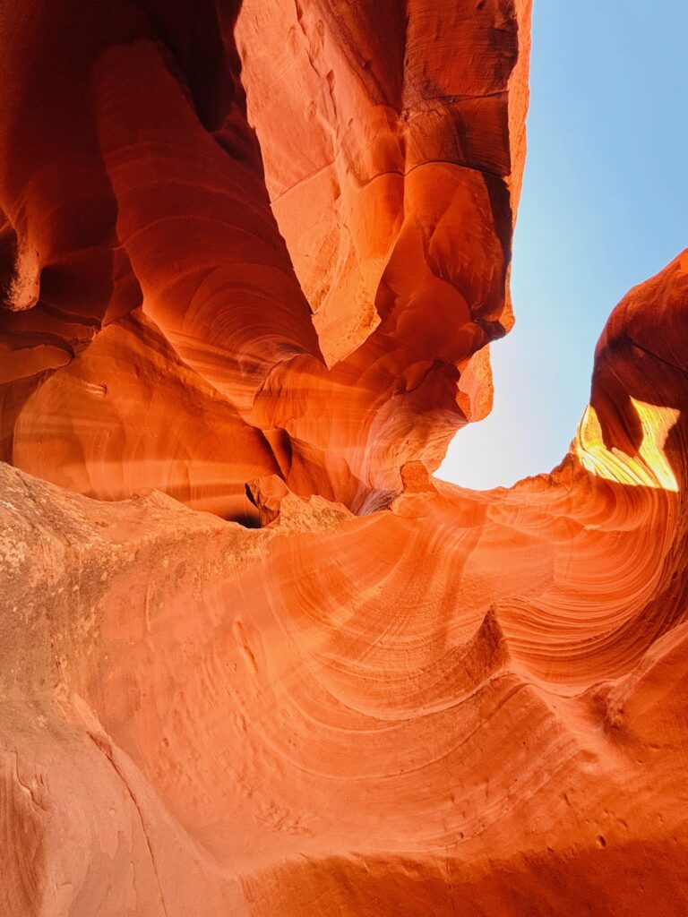 Vista verso l'alto dentro Antelope Canyon con pareti ondulate arancioni e rosse e apertura superiore con cielo azzurro
