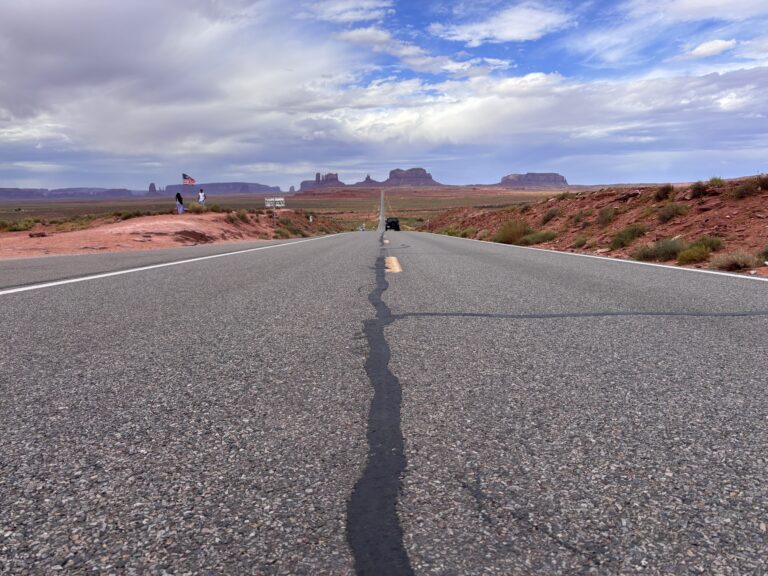 Highway 163 che si estende verso Monument Valley con buttes in lontananza e deserto rosso ai lati