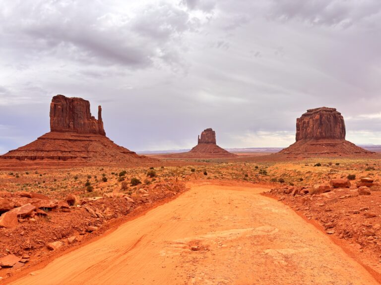 West Mitten Butte e Middle Butte in Monument Valley con strada rossa e deserto arancione al tramonto